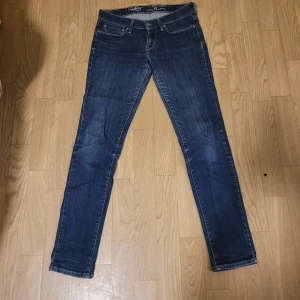 Levi's jeans i blå denim - Snygga Levi's jeans i klassisk blå denim. De har en slim passform och är perfekta för en stilren look. Jeansens design inkluderar de ikoniska Levi's-detaljerna med en läderpatch på baksidan och den röda Levi's-etiketten vid fickan.
