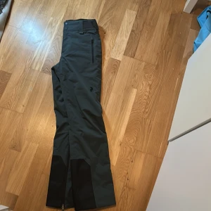 Mörkgrå skidbyxor från Peak Performance - Snygga mörkgrå skidbyxor från Peak Performance i storlek XS. Byxorna har dragkedjor vid bensluten och utrustade med Recco. Perfekta för skidåkning och utomhusaktiviteter. 