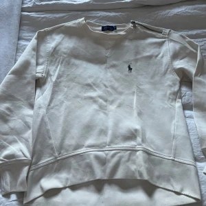 Vit tröja från Ralph Lauren - Säljer en stilren vit tröja från Ralph Lauren med en diskret logga på bröstet. Tröjan har en unik dragkedjedetalj vid halsen och långa ärmar. Perfekt för en avslappnad och snygg look.