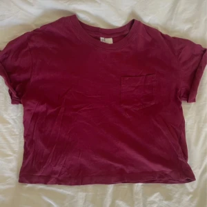 Vinröd t-shirt från H&M Divided - Snygg vinröd t-shirt från H&M Divided med en liten bröstficka. Den har en avslappnad passform och korta ärmar, perfekt för en casual look. Tillverkad i mjukt material.