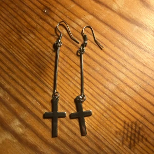 Silvriga korsörhängen - Snygga och stilrena örhängen i silver med hängande kors. Perfekta för att ge en edgy touch till din outfit. De har en enkel krok för enkel användning.