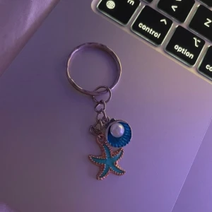 Nyckelring med sjöstjärna och snäcka - Charmig nyckelring med en turkos sjöstjärna och en blå snäcka med vit pärla. Perfekt för att ge en somrig touch till dina nycklar.