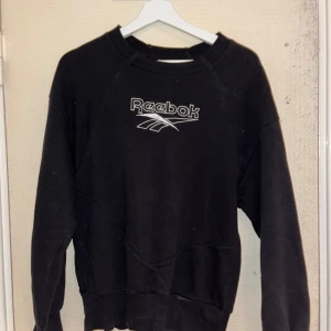 Svart sweatshirt från Reebok - Säljer en klassisk svart sweatshirt från Reebok med deras ikoniska logga på bröstet. Tröjan har långa ärmar och en rund halsringning, perfekt för en avslappnad stil.
