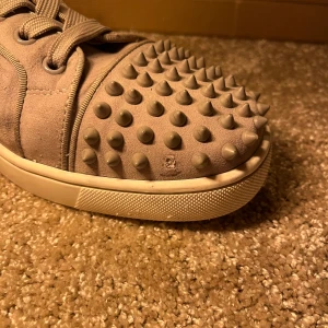 Christian Louboutin  - Snygga grå sneakers från Louboutin i mocka med coola nitar på tån och hälen. Skorna saknar en nit samt lite defekt i innerhäl. Extra nitar medföljer, samt skosnören, skohorn och dustbags!