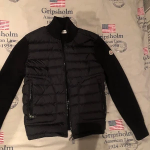 Svart dunjacka från Moncler - Snygg svart dunjacka från Moncler med dragkedja och ribbade ärmar. Jackan har ett stilrent märke på ärmen och är perfekt för kyligare dagar. Den är designad med en quiltad look och har praktiska fickor med dragkedjor den är k0pia men är som en äkta nfc funkar allt som det ska storlek s men passar xs