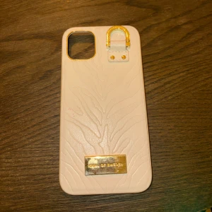Beige mobilskal från ideal of sweden - Elegant beige mobilskal från Ideal of Sweden med ett subtilt mönster och guldfärgade detaljer. I fint skick!