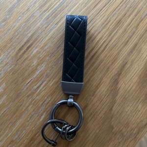 Svart nyckelring med quiltad design - Elegant svart nyckelring med quiltad design och metallbeslag. Perfekt för att hålla dina nycklar organiserade med stil.