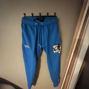 Blå mjukisbyxor med tryck - Snygga blå mjukisbyxor från  supply med unikt tryck på benet. Byxorna har snörning i midjan för justerbar passform och en avslappnad stil. Perfekta för en casual look.