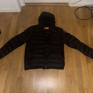 Svart dunjacka från Parajumpers - Säljer en svart dunjacka från Parajumpers, superlätt och perfekt för kyliga dagar. Jackan har en praktisk huva och dragkedja framtill. Den är designad för att hålla dig varm och bekväm.