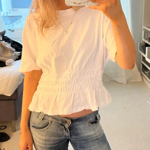 Vit blus med volangdetalj och resår i midjan  - Säljer en söt vit blus med elastisk midja och volangdetalj. Den har resår i midjan / indragen midja 