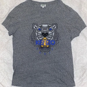 Grå t-shirt från Kenzo - Säljer en grå t-shirt från Kenzo. Kortärmad och tillverkad i mjukt material för extra komfort. T-shirten är använd några få gånger och har inga defekter. Den är i storlek L. 