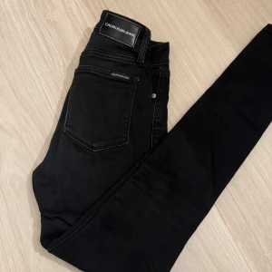 Svarta skinny jeans från Calvin Klein - Snygga svarta skinny jeans från Calvin Klein med hög midja. Klassisk femficksdesign med dragkedja och knapp framtill. Byxorna är använda men tyvärr blivit för små så köpt nya då dessa är så snygg på👌🏼ord.pris ca 1200kr