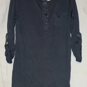 Grå tunntröja från Cubus, barn - Grå tunn tröja från Cubus med knappar framtill och en bröstficka. Tunn tröjan har trekvarts ärmar man kan förlänga och med knappdetaljer som man knäpper.. Perfekt för en avslappnad stil. Storlek 98