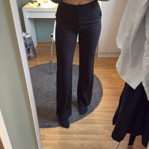 Svarta kostymbyxor - Snygga svarta kostymbyxor från Lindex med hög midja och rak passform. Perfekta för en stilren look. Byxorna har en klassisk design med dragkedja framtill. Modell Fiona tall, jag är 179cm