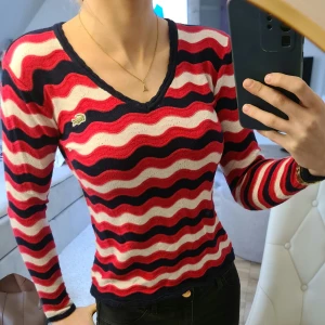 Randig tröja från Lacoste - Säljer en snygg randig tröja från Lacoste i rött, vitt och blått. Tröjan har en v-ringad hals och långa ärmar, perfekt för en stilren look. Den är tillverkad i ett mjukt material som känns skönt mot huden.