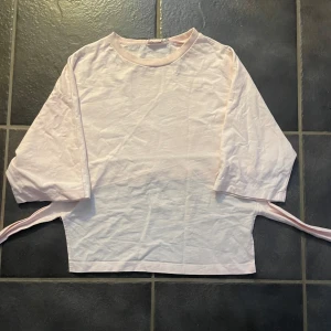 Ljusrosa topp med knytband - Säljer en ljusrosa topp med trekvartsärm och knytband i midjan. Perfekt för en avslappnad stil med en unik twist. Toppen har en lös passform och är tillverkad i ett mjukt material. Lappen är bort tagen av den gamla ägaren