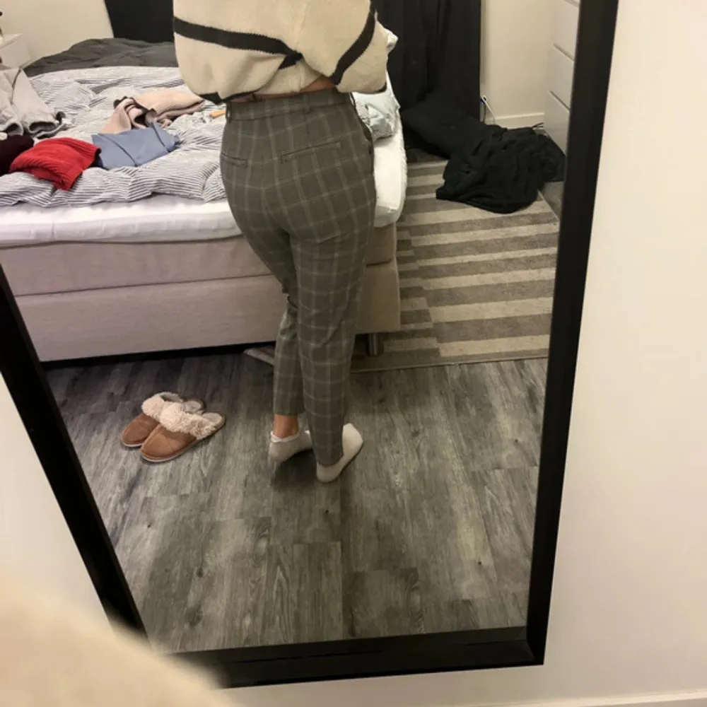 Snygga grå rutiga byxor från Lindex med en tight passform. De är högmidjade och perfekta för en stilren look. Byxorna har en klassisk design med dragkedja och knapp framtill.. Farkut & Housut.