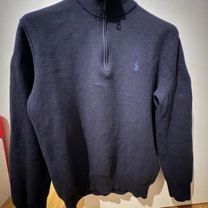 Ralph Lauren Quarter Zip - Snygg svart tröja från Ralph Lauren med halv dragkedja och broderad logga på bröstet. Perfekt för kyliga dagar med sin stilrena design och långa ärmar.