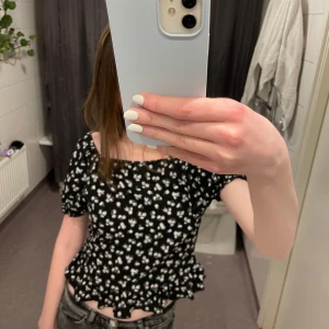 Topp - Säljer en söt svart topp m vita blommor 💕 den har korta puffärmar och en volangdetalj vid kanten. Bara använd några få ggr💕💕