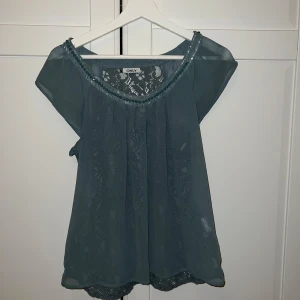 En blus från ONLY - Snygg turkos blus från ONLY med spetsdetaljer och korta ärmar. Perfekt för en stilren look med en touch av elegans. Blusen har en v-ringad design och är tillverkad i ett lätt och luftigt material. 💙