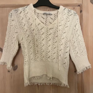 Beige stickad tröja med fransar - Säljer en beige stickad tröja från Zara med v-ringning och knytband. Tröjan har trekvartsärmar och fransdetaljer vid ärmslut och nederkant. Perfekt för en avslappnad stil.