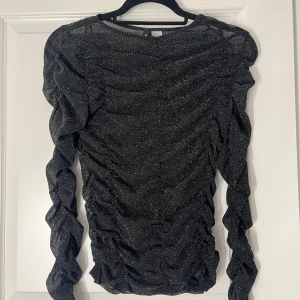 Svart glittrig topp  - Snygg svart glittrig topp med långa ärmar och rynkade detaljer. Använt en gång, jätte fin.