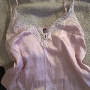 Ljusrosa satinlinne med spets - Säljer ett ljusrosa satinlinne från Divided med spetsdetaljer vid halsringningen.  Kan ha för att klä upp sig fint elr ett fint pjamaslinne🩷 köpte i prag.