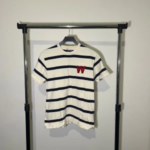 Randig t-shirt från Zara - Säljer en stilren randig t-shirt från Zara i vitt och marinblått. T-shirten har korta ärmar och ett rött 'W' broderat på bröstet. Perfekt för en avslappnad look.