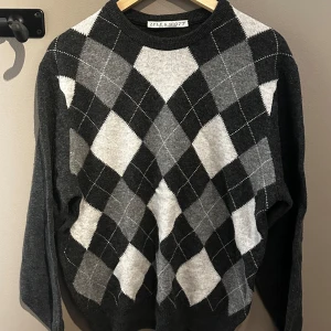 Grå rutig tröja från Lyle & Scott - Snygg grå tröja från Lyle & Scott med klassiskt rutmönster i olika nyanser av grått. Tröjan har långa ärmar och rund halsringning.