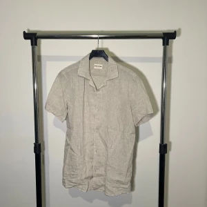 Beige linneskjorta från Skagen Clothing - Snygg beige kortärmad skjorta från Skagen Clothing i linne. Perfekt för varma dagar med sin lätta och luftiga känsla. Skjortan har knappar framtill och en klassisk krage.