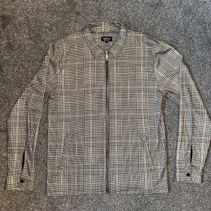 Rutig jacka från MAN - Snygg rutig jacka från BOOHOO-MAN i storlek L. Jackan har en dragkedja framtill och klassisk krage. Perfekt för en stilren look.