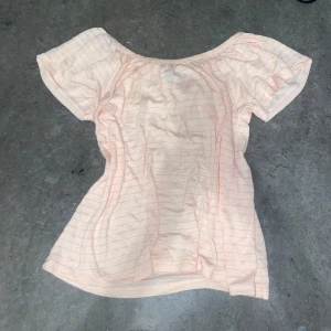 Ljusrosa randig offshoulder topp - Säljer en söt ljusrosa offshoulder topp med tunna ränder. Toppen har korta ärmar och en luftig passform, perfekt för varma dagar. Den är gjord i ett mjukt och bekvämt material.