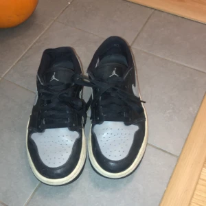 Nike Air Jordans i svart och grått - Säljer ett par klassiska Nike Air Jordans i svart och grått. Skorna har snörning och en ikonisk Air Jordan-logga på hälen. Perfekta för en stilren look.