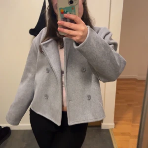 Grå kappa med knappar - Snygg grå kappa med dubbelknäppning och stilren design. Perfekt för kyligare dagar och ger en elegant touch till din outfit.