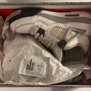 Nike Air Jordan sneakers - Säljer ett par Nike Air Jordan sneakers i vitt och grått med marinblå detaljer. Skorna har snörning och en ikonisk design med synlig luftdämpning i sulan.