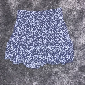 Blommig kortkjol i blått och vitt - Söt blommig kortkjol i blått och vitt med volangdetaljer. Perfekt för en somrig look!