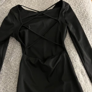Svart figursydd klänning med öppen rygg!  - Elegant svart klänning med långärmad design och unik snörning baktill. Perfekt för en stilren look. Säljer då den aldrig kommit till användning!☺️Storlek M men känns som en S 