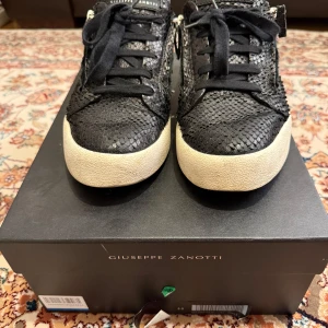 Svarta sneakers från Giuseppe Zanotti Frankie - Snygga svarta sneakers med textur från Giuseppe Zanotti. Skorna har snörning och en vit sula som ger en stilren kontrast. Perfekta för en trendig look. Detta är modellen med ormskinn. Storlek 44, box, påsen och kvittot finns givetvis kvar. Köpt på Farfetch. 