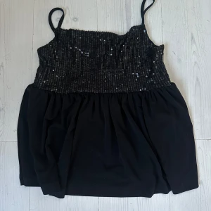 Svart paljettlinne stl 158/164 Gina Tricot - Snyggt svart linne med paljetter upptill och smala axelband. Använd 1 gång.