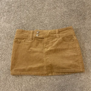 Beige  manchesterkjol från H&M - Snygg beige manchesterkjol från H&M i kort modell. Kjolen har två knappar framtill och praktiska fickor både fram och bak. Perfekt till både sommar och vinter!