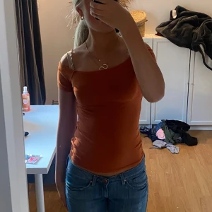 Brun offshoulder topp - Säljer en snygg orange offshoulder topp som är perfekt för både vardag och fest. Den är tight och sitter riktigt bra på kroppen. Toppen är i ett mjukt och stretchigt material, vilket gör den superbekväm att ha på sig. Passar perfekt till ett par jeans för en avslappnad look.