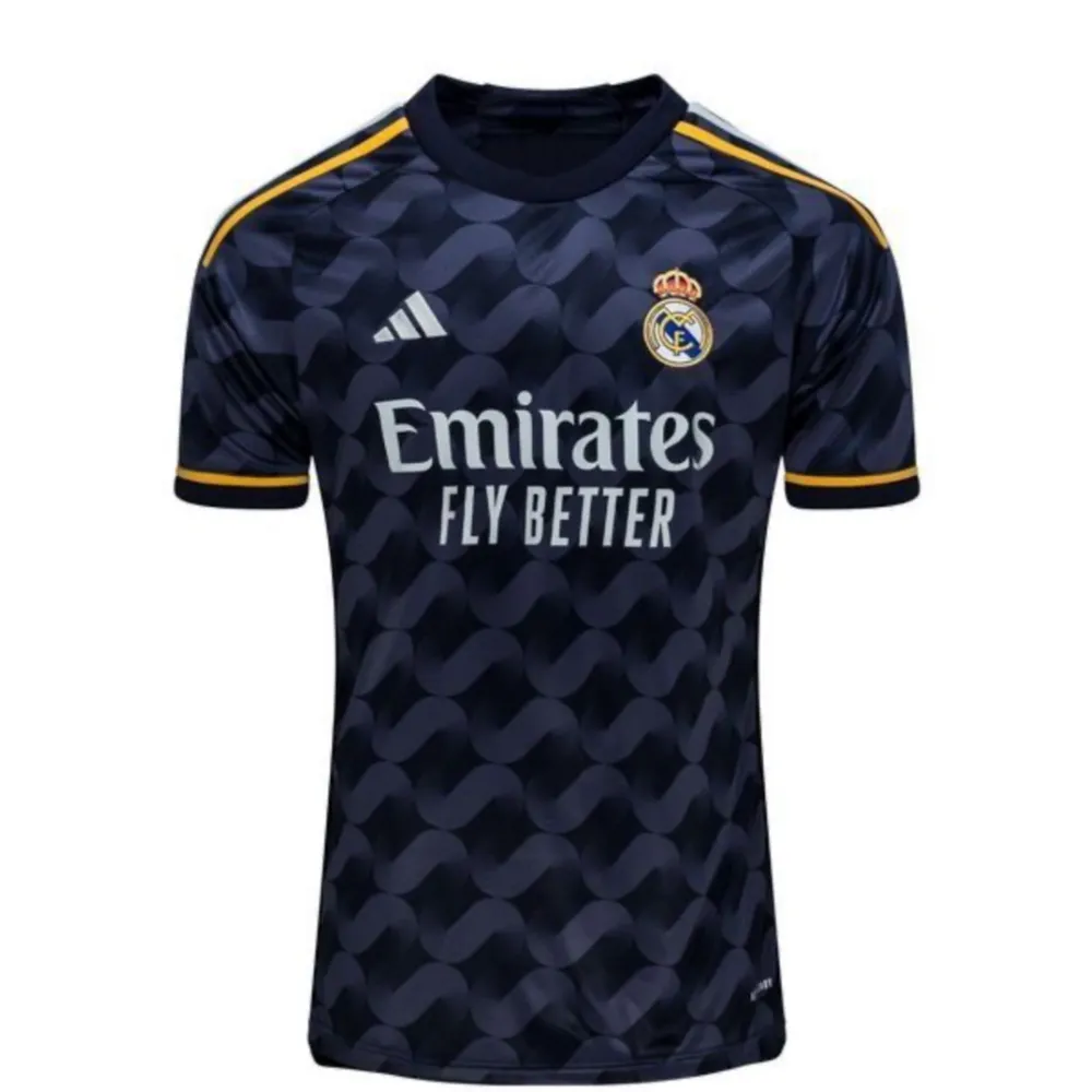 Säljer en snygg svart Real Madrid fotbollströja från Adidas. Tröjan har ett coolt mönster och gula detaljer på axlarna. Den är kortärmad och har klubbens emblem på bröstet. Perfekt för alla fans!. Shorts.