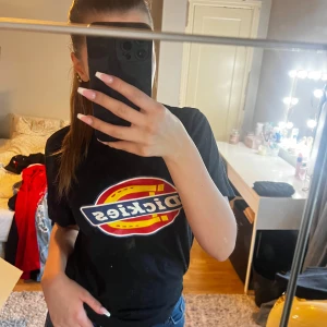 Svart t-shirt från Dickies - Säljer en svart t-shirt från Dickies med deras ikoniska logga i rött, gult och vitt på framsidan. Perfekt för en casual look och passar till allt. T-shirten är i bra skick och redo för nya äventyr! Trycket är dessvärre lite skadat. Ge gärna prisförslag 😊