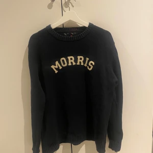 Mörkblå tröja från Morris - Säljer en snygg mörkblå tröja från Morris med texten 'MORRIS' i vitt på bröstet. Tröjan har en ribbad krage och långa ärmar, perfekt för en stilren look. Passar bra till både jeans och chinos.