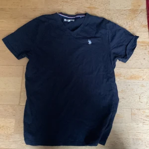 Svart t-shirt från U.S. Polo Assn. - Säljer en svart t-shirt från U.S. Polo Assn. med v-ringning och broderad logga på bröstet. Perfekt för en avslappnad stil. Passar M