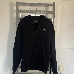 Svart tröja med dragkedja från Axel Arigato - Snygg svart tröja från Axel Arigato med halv dragkedja och tryckt logotyp på bröstet. Perfekt för en stilren look. Tröjan har långa ärmar och en bekväm passform.