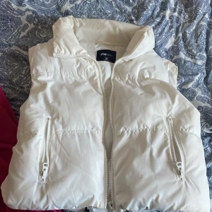 Vit dunväst från FB Sister,New Yoker - Säljer en snygg vit dunväst från FB Sister från New Yoker i storlek M. Västen har en dragkedja framtill och två praktiska fickor med dragkedjor. Perfekt för kyligare dagar när du vill hålla stilen.