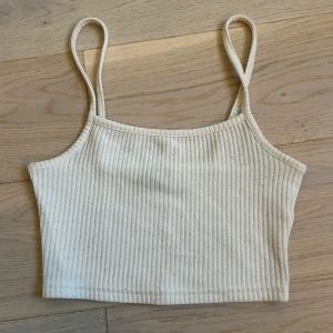 Beige ribbad linnetopp från H&M - Säljer en stilren beige ribbad linnetopp från H&M i storlek XS. Toppen har smala axelband och en croppad passform, perfekt för varma dagar. Enkel och snygg design som passar till det mesta. Toppen är såklart använd och tvättad och är därför lite nopprig