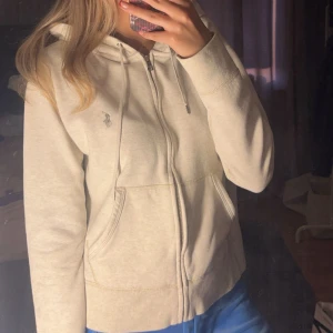 Beige hoodie från Polo Ralph Lauren - Säljer en stilren beige hoodie från Polo Ralph Lauren. Den har dragkedja framtill och en klassisk logga broderad på bröstet. Perfekt för en avslappnad look. 🧥