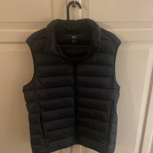 Svart dunväst från Uniqlo - Snygg svart dunväst från Uniqlo med dragkedja framtill. Perfekt för lager-på-lager under kyliga dagar. Hör av dig vid frågor!